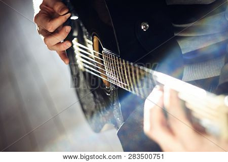 A Person Plays A Black Glossy Guitar, Illuminated By Bright Sunlight, While Holding A Mediator In Hi
