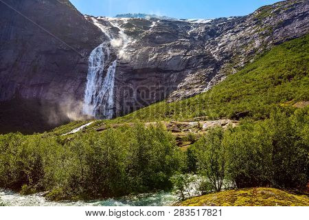 Waterfall And Green Trees On The Way To Briksdal Or Briksdalsbreen Glacier In Olden, Norway