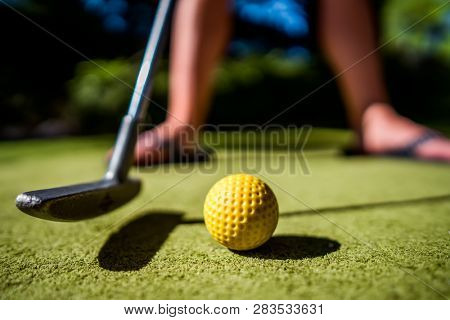 Mini Golf yellow ball with a bat near the hole at sunset