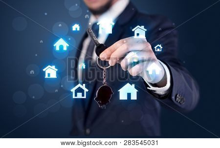 Businessman in suit holding keys with house graphics around and dark background