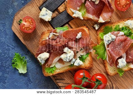 Bruschetta With Prosciutto, Salad Frieze And Cheese On The Kitchen Table. Snack. View From Above.