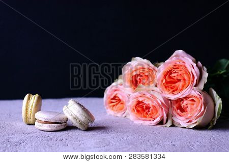 A Stack Of Macaroons With A Bouquet Of Beautiful Peach-colored Roses On A Gray Concrete Background.