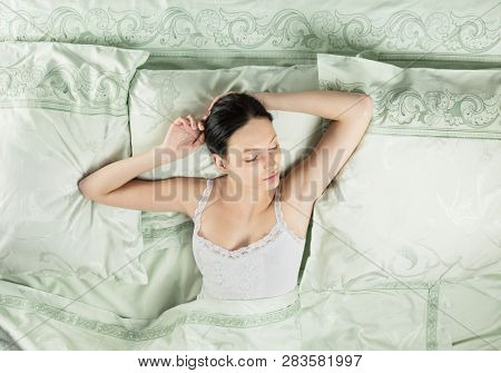 Beautiful young woman sleeping in luxury bed. Bed is made with linen embroidered percale.