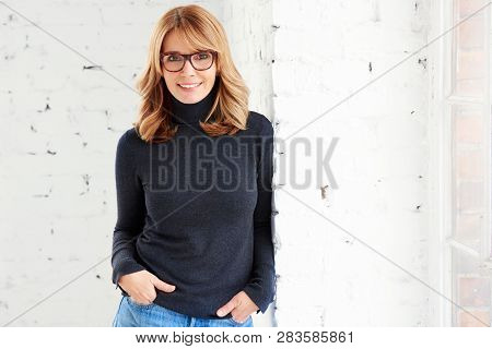Portrait Of Attractive Woman Wearing Roll Neck Sweater And Jeans While Looking At Camera And Smiling