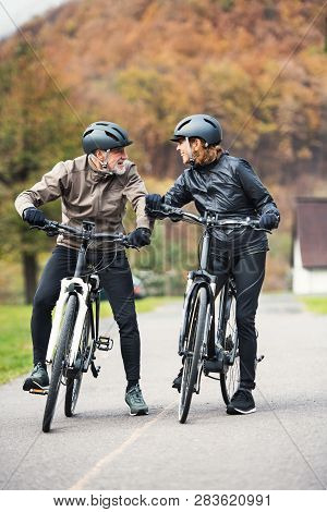 Active Senior Couple With Electrobikes Standing Outdoors On A Road In Nature.
