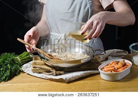 The Chef Pours White Wine Into An Italian Risotto. Shrimp, White Wine, Rice, Onions, Thyme, Garlic. 