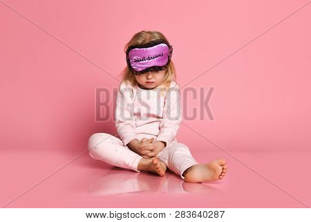 Studio Shot Of Pleased Beautiful Little Girl Posing In Eyemask. Cheerful Kid Girl In Pajamas Seating