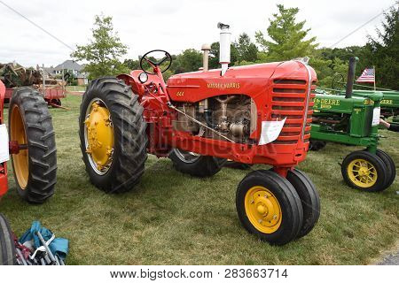 A Row Of Vintage Farm Machinery Tractors Including Red Massey Harris And Green John Deere On Display