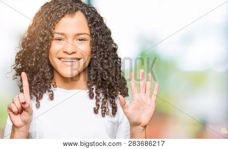 Young beautiful woman with curly hair wearing white t-shirt showing and pointing up with fingers number six while smiling confident and happy.