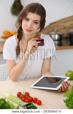 Young  Woman Looking For A New Recipe For  Cooking In A Kitchen. Housewife Is Making Online Shopping