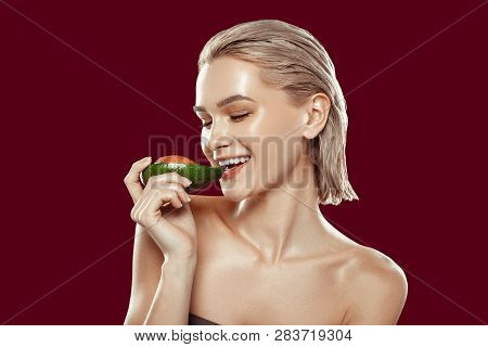Cheerful Blonde-haired Model Biting Avocado While Posing With It