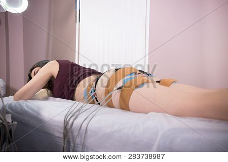 Cosmetology Beauty Clinic. Young Woman Taking Myostimulation, Lying In Bed At The Nutritionists Offi