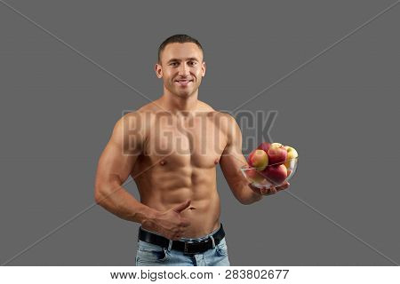 Charming, Cheerful Bodybuilder Smiling, Holding Bowl With Apples. Muscular, Sexy Man With Naked Tors