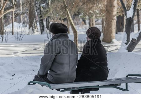 A Married Couple Of Pensioners Is On The Gray Bench In The Snow Park In Winter And An Elderly Woman 