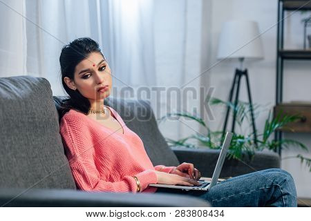Upset Indian Woman With Bindi Using Laptop On Sofa