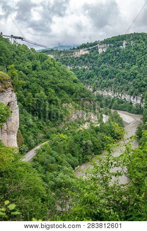 Skybridge Suspension Bridge Over A Gorge Over An Abyss With A River And Serpentine Road On A Cloudy 