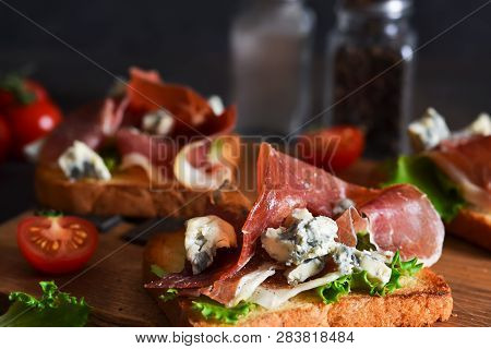 Bruschetta With Prosciutto, Salad Frieze And Cheese On The Kitchen Table. Snack.