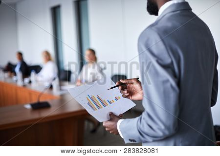 Young Elegant Economist Holding Paper With Financial Chart While Making Report For Colleagues At Con