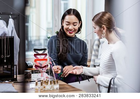 Dark-haired Smiling Asian Woman In A Navy Polo Neck Testing A New Perfume