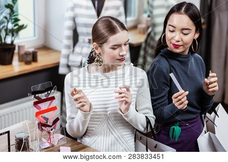 Smiling Pretty Long-haired Woman In A White Sweater Enjoying A New Perfume