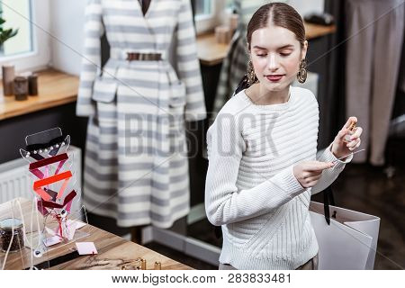 Smiling Pretty Long-haired Woman In A White Sweater Smelling Her Wrist