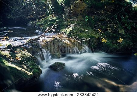 Long Exposure Of A River Creek With A Small Waterfall. Sunset And Strong Detail Bokeh View. Blue Cal