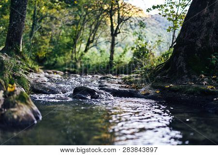 A River Creek With A Small Waterfall. Sunset And Strong Detail Bokeh View. Blue Calm Warm Water