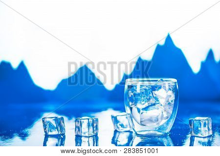 Double Wall Glass Of Clear Water On A Cold Background With Ice Cubes And Mountain Peaks. Drinking Fr