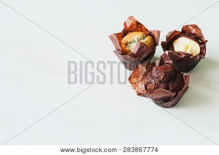 Three Different Muffins On A White Background. Chocolate, Bluberry And Brownie Cheesecake Muffins.