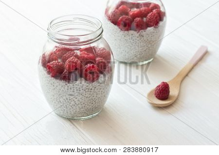 Chia Seeds Pudding With Coconut Milk And Raspberry In Glass Jars. Wooden Spoon With Berry In White W