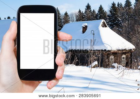 Travel Concept - Tourist Photographs Of Snow-covered Old Rural Houses At The Edge Of Forest In Winte