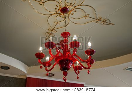 Glass Red Chandelier In The Room, Mounted On A Patterned Ceiling