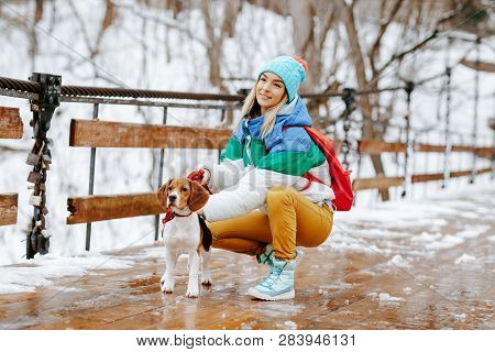 Portrait Of Cheerful Young Woman In Warm Stylish Clothes And Bagpack Posing With Her Beagle Dog On T