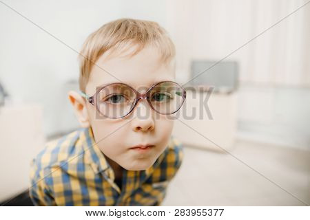 Child Boy Squints In Glasses For Eyes Of Sight, Looks Into Frame. Concept Reception Ophthalmologist.
