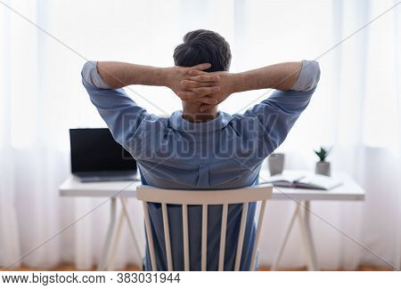 Home Office Relax. Rear View Of Male Freelancer Resting At Workplace, Leaning Back On Chair With Han