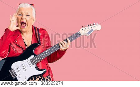 Senior beautiful woman with blue eyes and grey hair wearing a modern look playing electric guitar shouting and screaming loud to side with hand on mouth. communication concept. 
