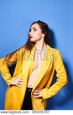 A Beautiful Girl Poses In A Yellow Coat Against A Blue Wall