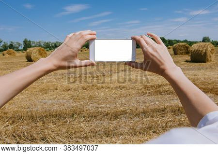 Mockup Of A Smartphone In The Hands Of A Girl. Against The Background Of A Field With Bales Of Hay.