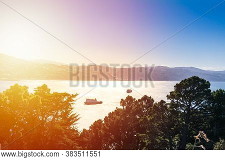 Sun Set Beams Over Wellington Harbour As An Interisland Ferry Approaches The Port And A Small Cargo 