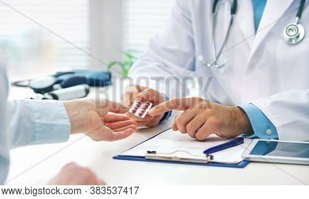 Doctor consulting female patient about pills and dicsussing health treatment sitting in the office at the desk. Medicine and health care concept