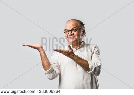 Portrait Of Cheerful Indian Senior Old Man Pointing Or Presenting Or In Hands Folded Pose