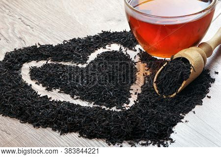 Concept I Like Tea. A Cup Of Black Tea And Dry Black Tea Leaves On A Wooden Table. Heart Symbol Made