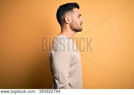 Young handsome man wearing casual sweater standing over isolated yellow background looking to side, relax profile pose with natural face with confident smile.