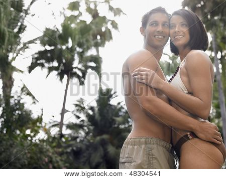 Widok z boku o pół ubrany młoda para stojący przed drzewa i niebo