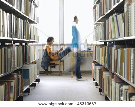 Vista lateral de uma jovem estudante masculino fazendo lição de casa, na biblioteca