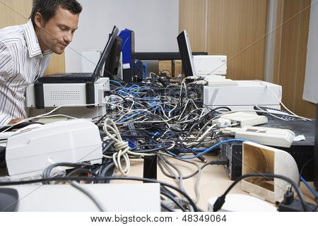 Vista lateral de un oficinista masculino mirando el lío de cables conectar computadoras e impresoras en la oficina