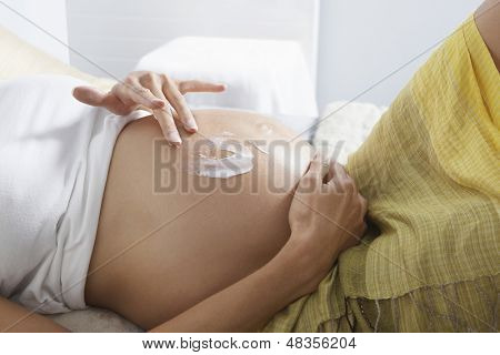 침대에서 위에 로션을 바르는 임신한 여자의 중앙부