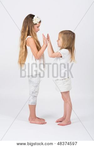 Duas meninas vestidas de branco jogando bater uns aos outros em mãos