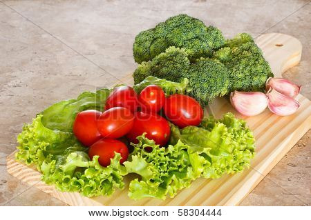 Broccoli, Tomatoes, Salad And Garlic On Wooden Board