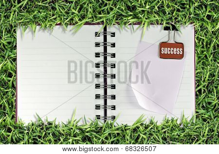 blank page of note book on grass and Binder Clip